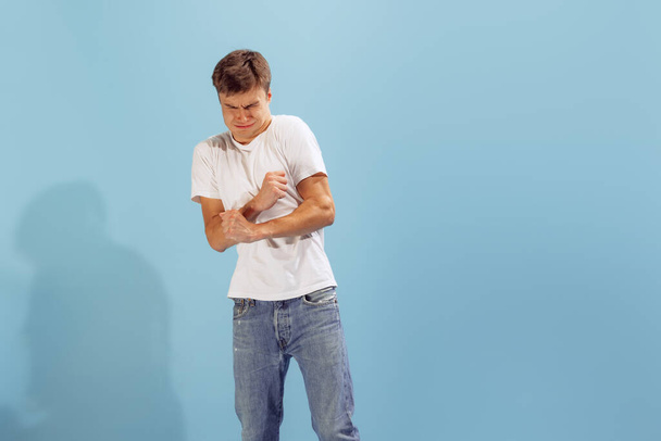 Portrait of young man in casual clothes showing emotions of disgust isolated over blue background. Unpleasant feelings. Concept of emotions, facial expression, lifestyle, fashion, youth - Foto, afbeelding