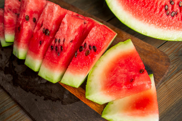 Watermelon cut into small triangles on a wooden board. On a wooden table is a board with slices of watermelon. Sweet slices of watermelon with bones. - Φωτογραφία, εικόνα