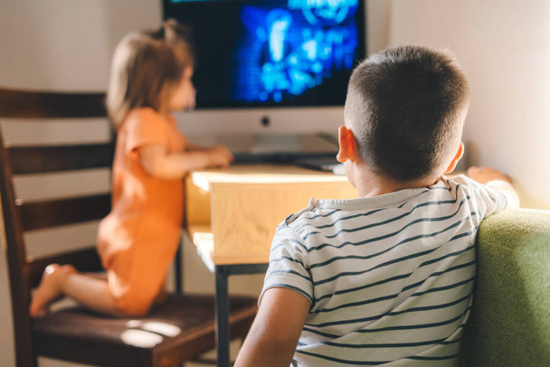 Brother and baby sister watching TV at home. Kids enjoying free time watching videos. New technology education concept - 写真・画像