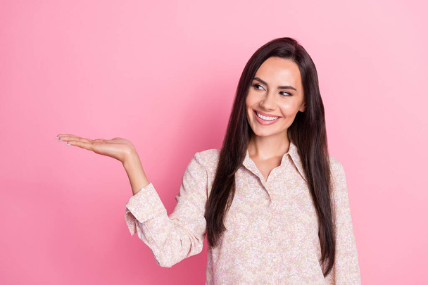 Photo of young attractive cute smiling woman interested looking hold hand product promoter isolated on pink color background. - Фото, зображення