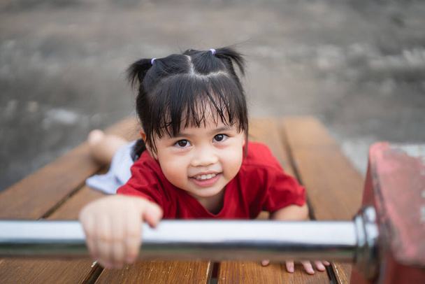 Cute asian girl play on school or kindergarten yard or playground. Healthy summer activity for children. Little asian girl climbing outdoors at playground. Child playing on outdoor playground. - 写真・画像