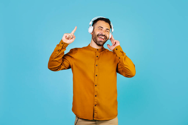 Cheerful middle eastern man listening to music with wireless headphones and singing. High quality photo - Foto, imagen