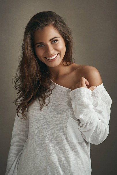 Уверенность хорошо сочетается с любой одеждой. Портрет красивой молодой женщины, улыбающейся на коричневом фоне в студии - Фото, изображение