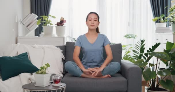 Jonge Aziatische vrouw dragen casual site op bank start meditatie doen yoga gevoel kalm en ontspannen verfrissende start nieuwe dag in woonkamer indoor planten thuis. Levensstijl tiener activiteit concept. - Video