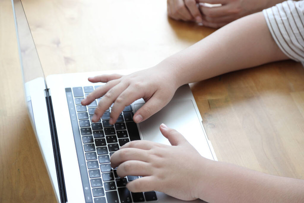 El primer plano de las manos del niño usando el ordenador portátil en casa. - Foto, imagen