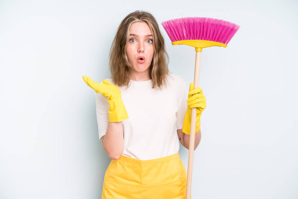 caucasian pretty woman looking surprised and shocked, with jaw dropped holding an object. housekeeper cleaning concept - Photo, Image
