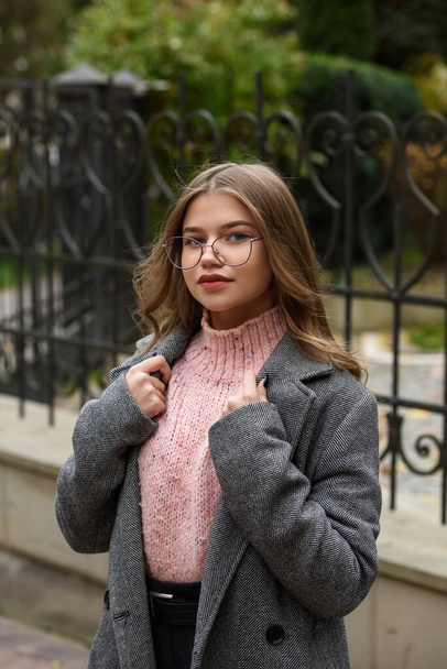 young beautiful girl posing on the street. Dressed in a stylish gray coat, knitted pink sweater and skirt. - Photo, Image