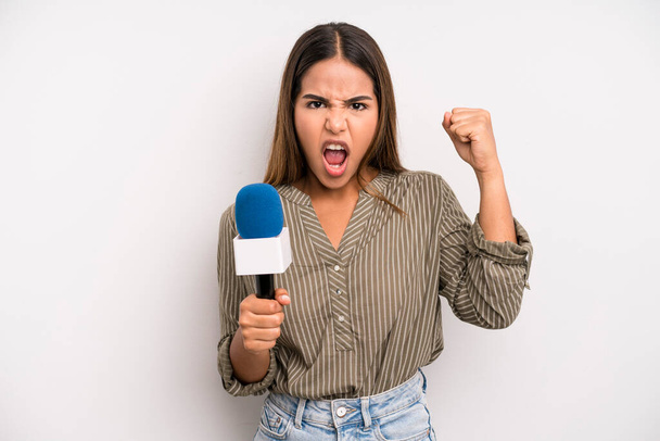 hispanic pretty woman shouting aggressively with an angry expression. presenter with a microphone concept - Foto, Imagem