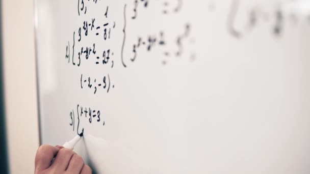 Young adult woman teacher in glasses is explaining maths topic to students online in the cabinet in minimalism style with white walls and whiteboard. - Materiał filmowy, wideo