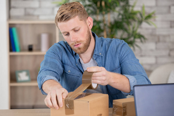 man wrapping a box while he is moving home - Photo, image