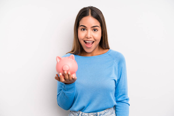 hispanic pretty woman looking happy and pleasantly surprised. piggy bank concept - Zdjęcie, obraz