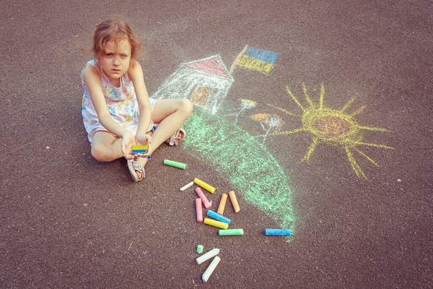 Ukrainian girl child draws children's drawings with chalk on the pavement. - 写真・画像