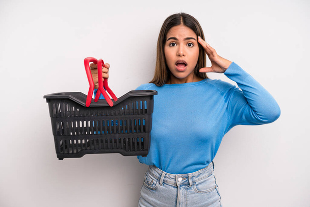 hispanic pretty woman looking happy, astonished and surprised. empty supermarket basket concept - Photo, image