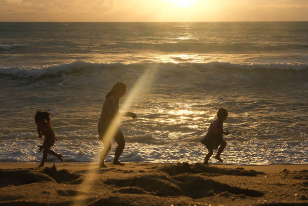 Ευτυχισμένη ασιατική οικογένεια της μητέρας και των κορών που διασκεδάζουν παίζοντας στην παραλία κατά τη διάρκεια των καλοκαιρινών διακοπών στο ηλιοβασίλεμα. Οικογενειακό καλοκαιρινό ταξίδι στην παραλία. έννοια ταξίδια και διακοπές. - Φωτογραφία, εικόνα