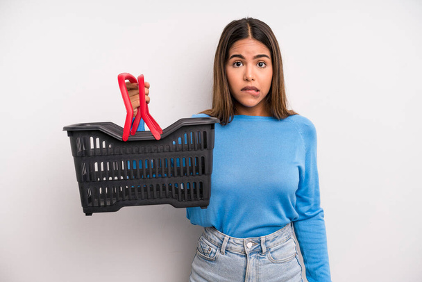 hispanic pretty woman looking puzzled and confused. empty supermarket basket concept - Fotó, kép