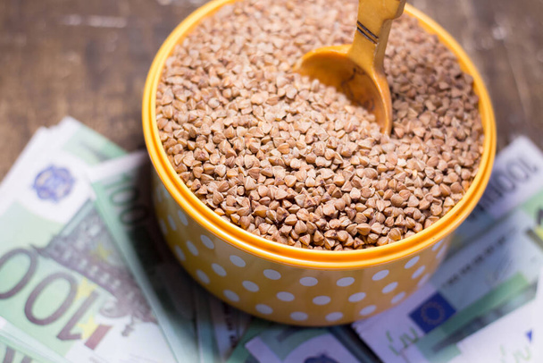 Buckwheat in a bowl with a wooden spoon on dollar bills. Rising prices in Ukraine due to the war - Photo, Image