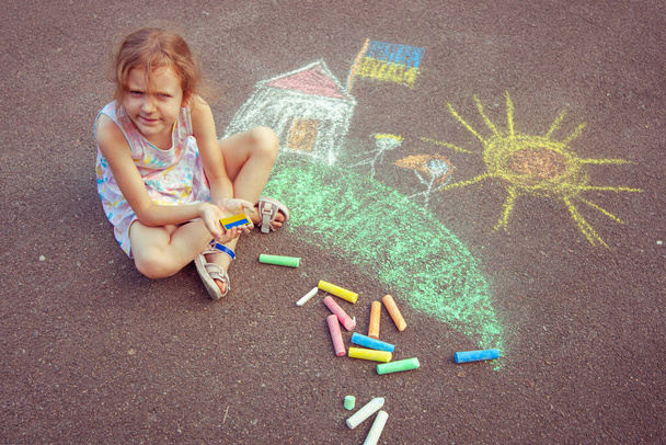 Ukrainian girl child draws children's drawings with chalk on the pavement. - Photo, image