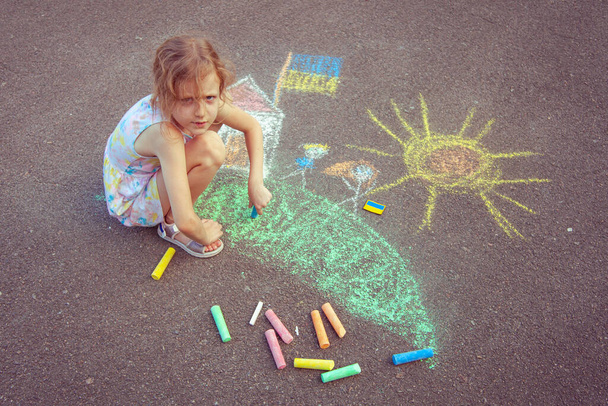 Ukrainian girl child draws children's drawings with chalk on the pavement. - Foto, imagen