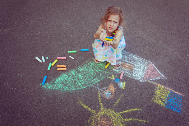 Ukrainian girl child draws children's drawings with chalk on the pavement. - Fotó, kép