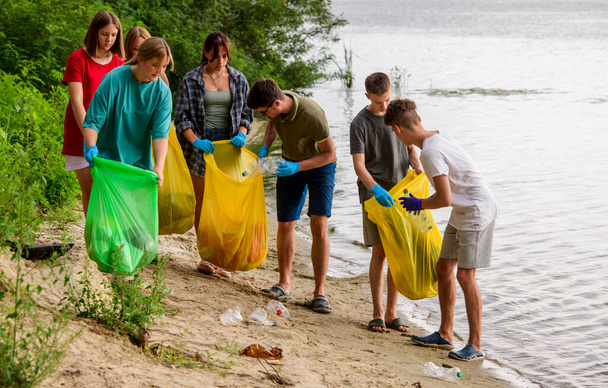 a team of teenagers collect garbage on the river bank - Fotografie, Obrázek