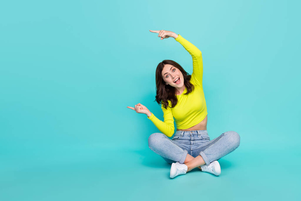 Full body photo of crazy cheerful lady sit floor indicate fingers empty space isolated on turquoise color background. - Fotografie, Obrázek