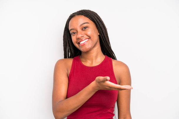 black young adult woman smiling cheerfully, feeling happy and showing a concept in copy space with palm of hand - Fotoğraf, Görsel