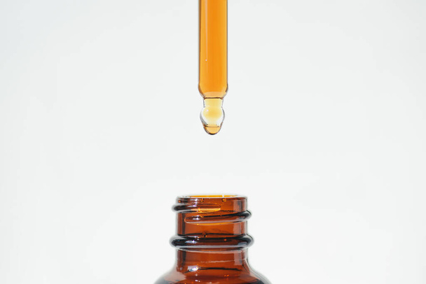 A drop of liquid falling from a pipette into an amber bottle. Skincare products, natural cosmetic on white background. Beauty concept for face and body care. - Photo, Image