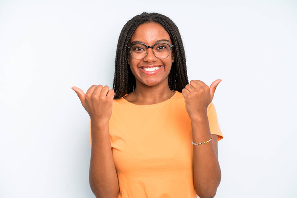 black young adult woman smiling joyfully and looking happy, feeling carefree and positive with both thumbs up - 写真・画像