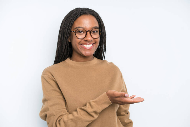 black young adult woman smiling cheerfully, feeling happy and showing a concept in copy space with palm of hand - Foto, afbeelding