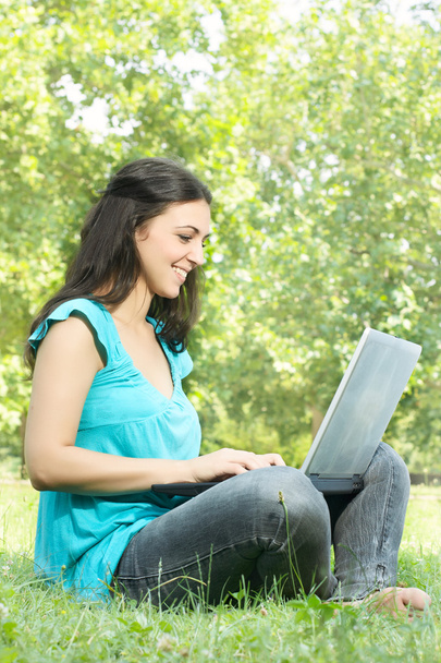 Porträt eines süßen Mädchens, das mit einem Laptop auf dem Rasen im Park sitzt - Foto, Bild