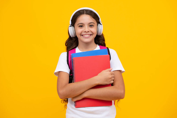 Iskolás lány, tinédzser hallgató fülhallgatóban könyveket tart sárga, elszigetelt stúdió háttérről. Iskolai és zeneoktatási koncepció - Fotó, kép