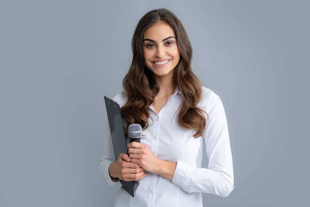 Young female journalist or businesswoman with microphone and clipboard on gray background - 写真・画像