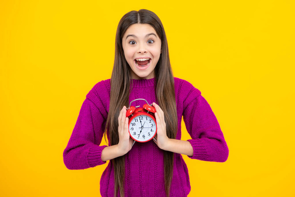Excited face. Teen student girl hold clock isolated on yellow background. Time to school. Teenager child with alarm clock showing time, late awakening. Amazed expression, cheerful and glad - Valokuva, kuva