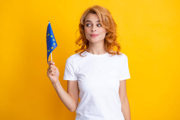 Ευτυχισμένη κοκκινομάλλα που κρατά τη σημαία της ένωσης της Ευρώπης, απομονωμένη στο κίτρινο - Φωτογραφία, εικόνα