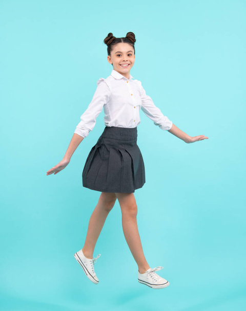 Full length jump of teenager girl on blue isolated studio wear casual skirt and shirt. Funny school girl, amazed kid genius, excited young student. Happy teenager, positive and smiling emotions - Foto, afbeelding