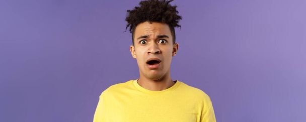 Close-up portrait of shocked, alarmed young man gasping, open mouth scared and frightened, staring camera concerned, facing troublesome shocking news, purple background. Copy space - Photo, image
