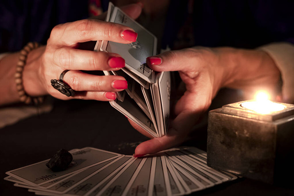 Fortune teller female hands shuffling a deck of tarot cards, during a reading. Close-up with candle light, moody atmosphere. - Photo, image