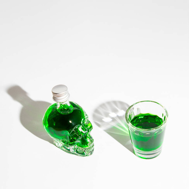 Poisonous green liquor in crystal skull bottle and glass. Halloween party background. - Фото, изображение