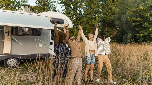 Group of happy young best friends, standing in nature, raising and holding each others hands after reaching the destination of their camping van road trip. High quality photo - Foto, imagen