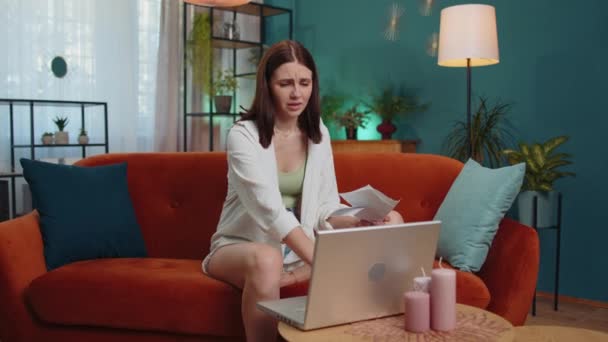 Stressed girl at home room looking at unpaid bank debt bills, doing paperwork, planning budget, calculate finances mortgage payments. Displeased young woman throws paper bills sitting on orange couch - Imágenes, Vídeo