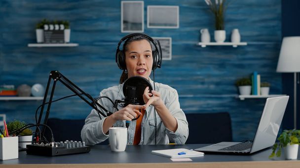 Digital content creator in studio at home recording daily vlog while telling stories. Creative social media influencer presenting to audience world events while sitting in studio living room. - Foto, imagen