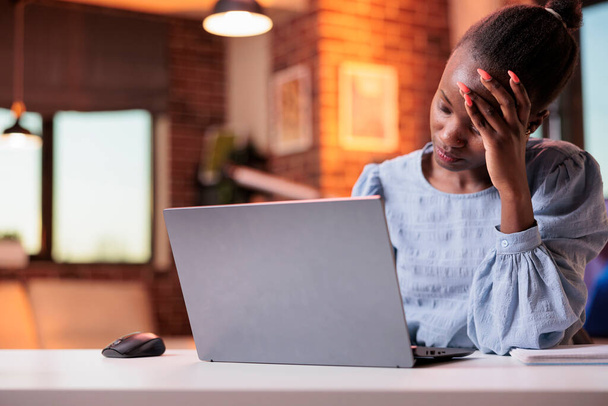 Stressed young female freelancer having headache and working on laptop, corporate employee burnout concept. Tired busy african american businesswoman, unhappy employee at workplace - Fotoğraf, Görsel