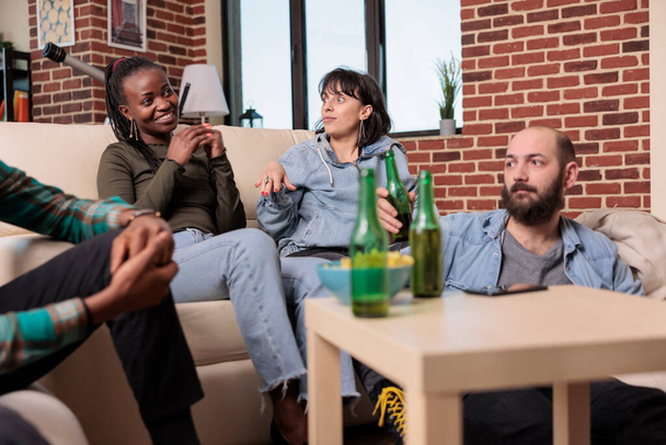 Diverse group of friends laughing and having conversation at fun gathering, drinking bottles of beer. People bonding and talking about leisure activity, enjoying friendship event. - Photo, image