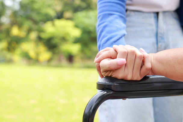 Ένας φροντιστής σφίγγει το χέρι ενός ηλικιωμένου που κάθεται σε αναπηρικό καροτσάκι. Νοσηλευτικές έννοιες για τη φροντίδα της υγείας των ηλικιωμένων, κέντρο αποκατάστασης της υγείας. παιδί που φροντίζει την ηλικιωμένη μητέρα - Φωτογραφία, εικόνα