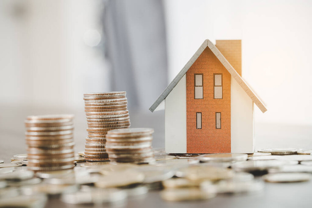 House model and money coins stacks on blur table background. Savings plans for home, loan, investment, mortgage, finance and banking about house concept. - 写真・画像