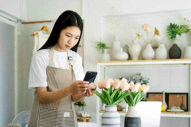Happy asian female, small stock business owner holding phone product photography checking commercial shipping delivery order on smartphone using mobile app technology. - Photo, image