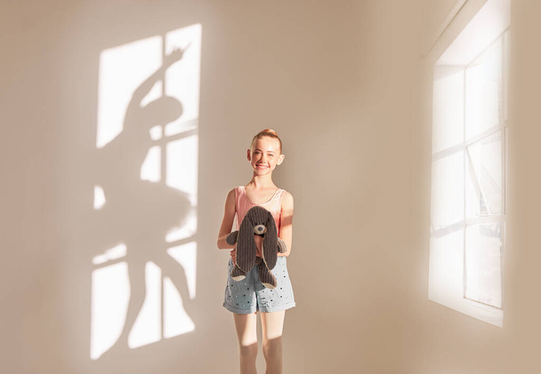 Creative art and dance with a girl dreaming of ballet with motivation and goal of becoming dancer in a studio with a teddy bear. Shadow of a ballerina or dancer on a wall with a kid next to a window. - Foto, imagen
