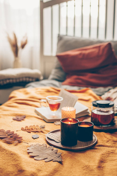 Open book, burning candles and herbal tea in glass cup on yellow plaid on bed in cozy bedroom. Reading, relaxation, recreation at home. Aututmn mood. - Fotografie, Obrázek