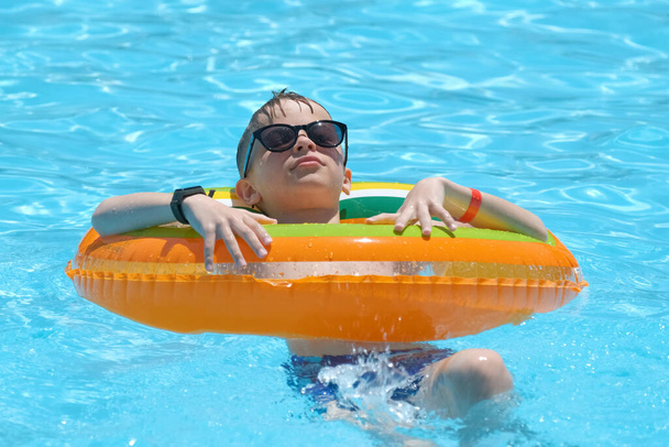 Portrait of happy child boy relaxing in inflatable circle in swimming pool on sunny summer day during tropical vacations. Summertime activities concept. - Fotó, kép