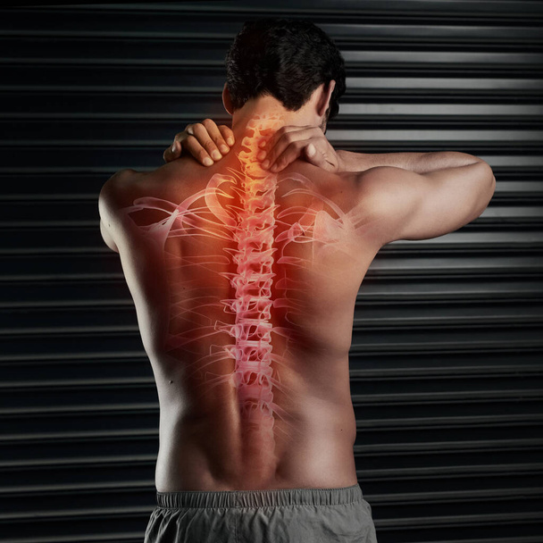 Не рискуйте повреждением позвоночника. Студийный снимок мускулистого молодого человека, массирующего шею позвоночником, показывающего через компьютеры - Фото, изображение